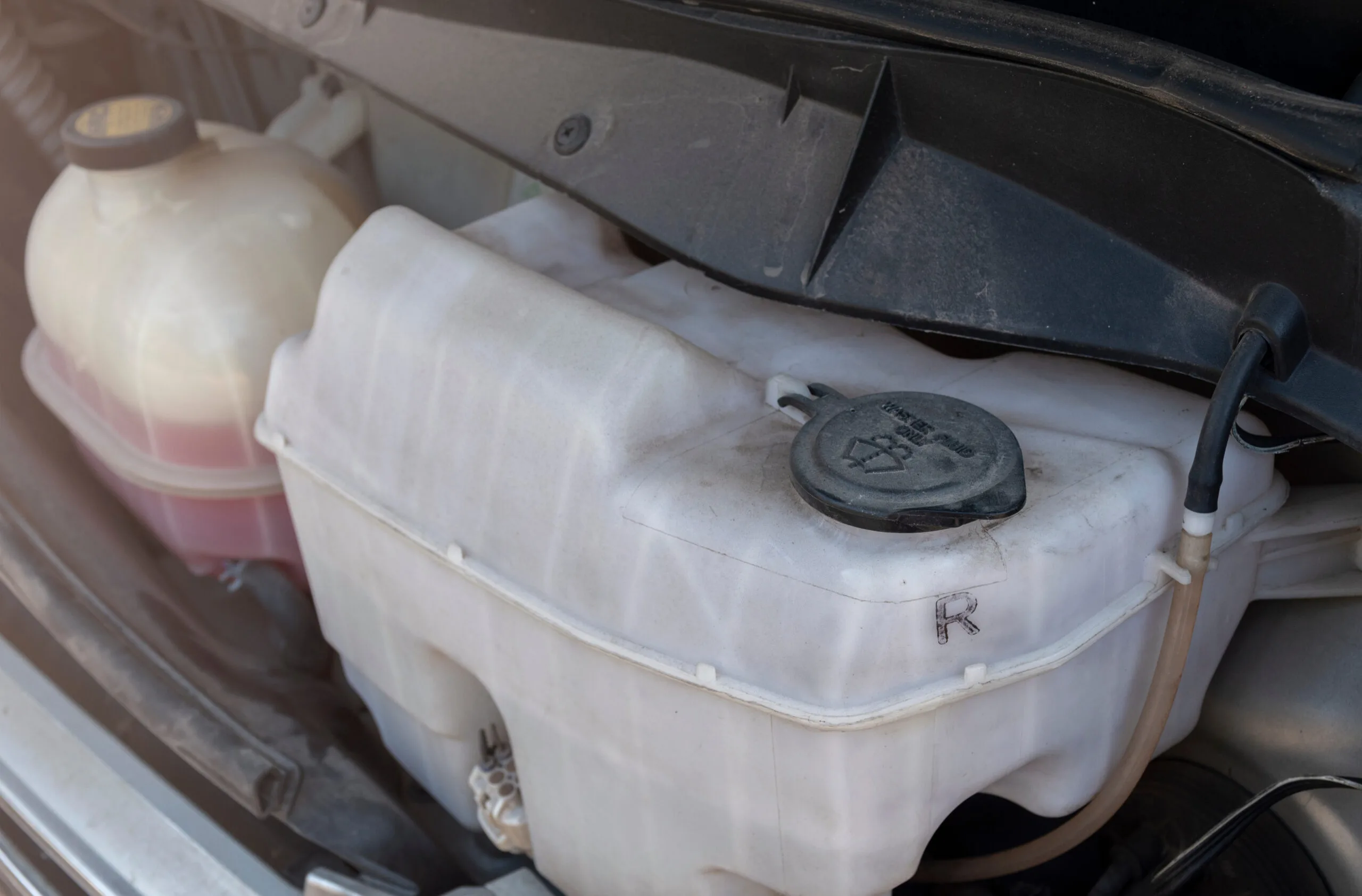 Close-up of truck parts: Windshield washer fluid reservoir and coolant tank under the hood.
