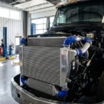 Photograph of a semi-truck's exposed engine bay with a large aluminum charge air cooler and blue silicone hoses.